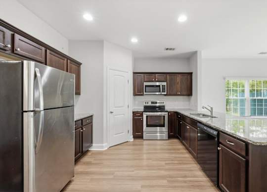 A kitchen with a refrigerator, microwave, oven, and sink.