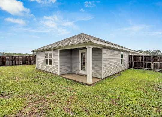 A small house with a grey roof and a white door is surrounded by a wooden fence.