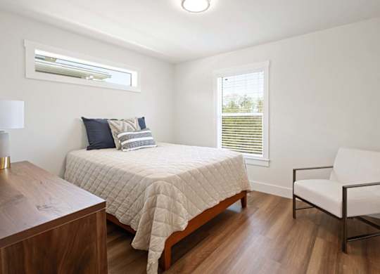 A bedroom with a bed, chair, and window.