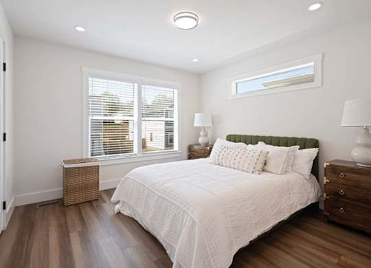 A bedroom with a large bed, a window with blinds, and a wooden floor.