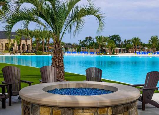 Houses for Rent in Humble, TX - Edgewater at the Lagoon - Poolside Fire Pit with Adirondack Chairs on Smooth Concrete, Next to Grass Lawn with Palm Tree, and View of the Expansive Sundeck.