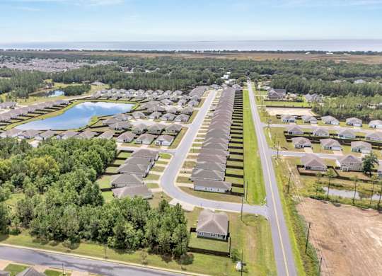 A bird's eye view of a residential area with houses, a lake, and a road.