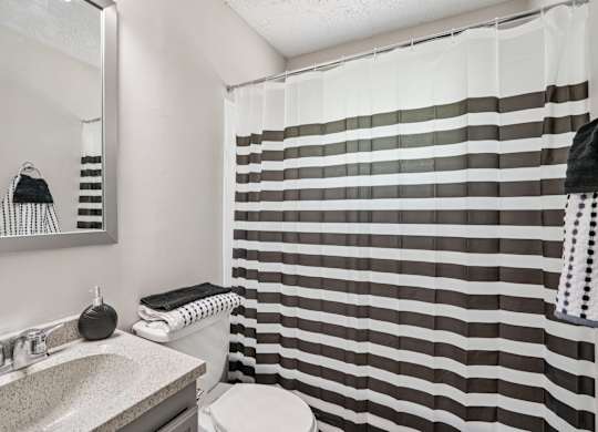 A bathroom with a striped shower curtain and a round shower head.