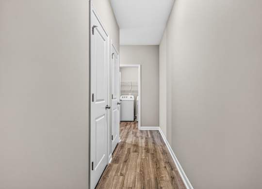A long hallway with a white door on the left and a white trash can in the distance.