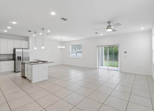 A spacious kitchen and living room with white tile flooring and ceiling.