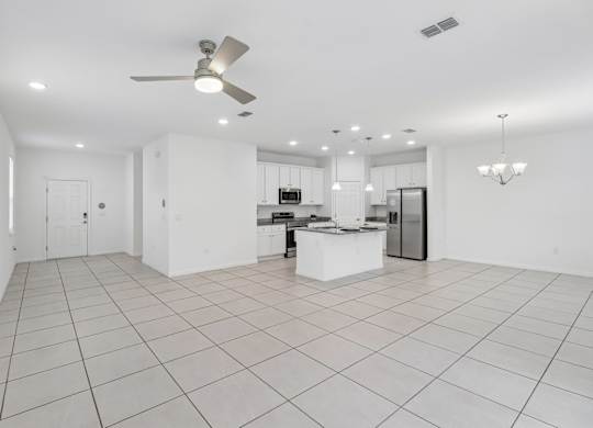A spacious kitchen and living room with white tiled floors and white walls.
