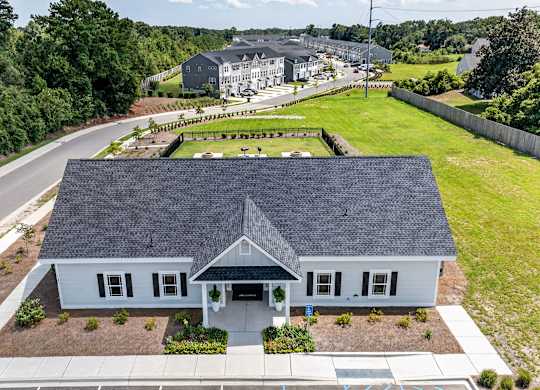 A house with a grey roof and white walls is surrounded by a well-maintained lawn and a road.