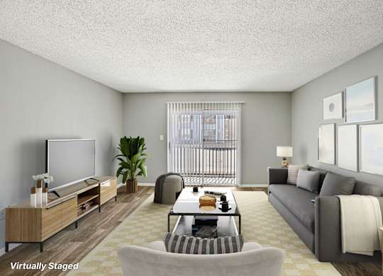 A living room with a grey couch, a wooden entertainment unit, and a large window with a view of a balcony.