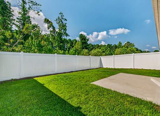 A white fence separates a green lawn from a concrete path.
