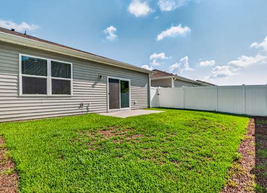 A house with a grey siding and a green door is surrounded by a white fence and has a green lawn.