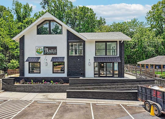 A small white building with a black roof and a sign that says "The Trails".