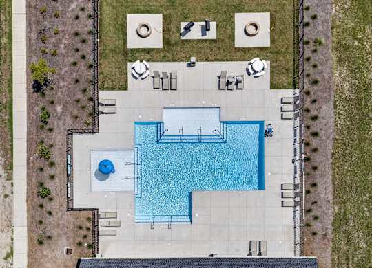 An aerial view of a pool surrounded by a concrete patio and a grassy area.