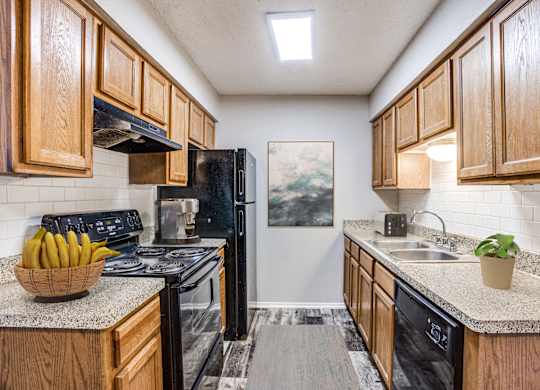 Apartments for Rent in Fort Worth- Monarch Pass- Kitchen with Black Appliances, Wooden Cabinets, and Tile Backsplash