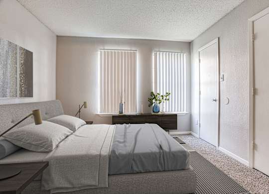 Fort Worth TX Apartments - Monarch Pass - Bedroom with Wall-to-wall Plush Carpeting, Beige Walls, Large Bed, and Windows with Vertical Blinds