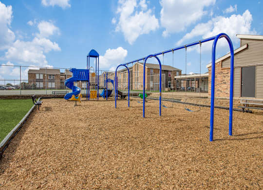 Pet-Friendly Apartments in Fort Worth TX - Monarch Pass - Playground with Swings, Slide Tower, and View of Apartment Buildings