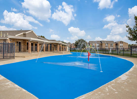 Apartments In Fort Worth, TX - Monarch Pass - Gated Splash Park with Apartment Buildings in the Background.