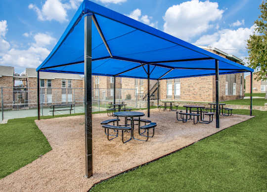 Fort Worth Apartments for Rent - Monarch Pass - Covered BBQ Area with Round Tables, Benches, and View of Sports Court and Apartment Buildings