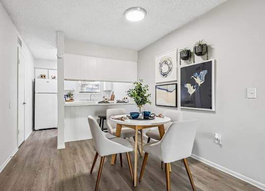 A dining room with a table set for two and a kitchen in the background.