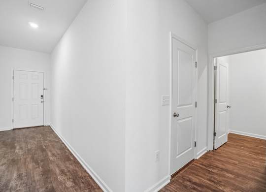 A room with white walls and wood flooring with three doors.