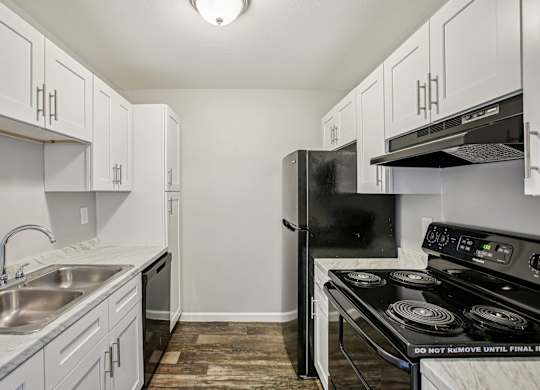 A kitchen with a black fridge and stove top oven.