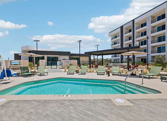 A large outdoor swimming pool with lounge chairs and umbrellas in front of a modern building.