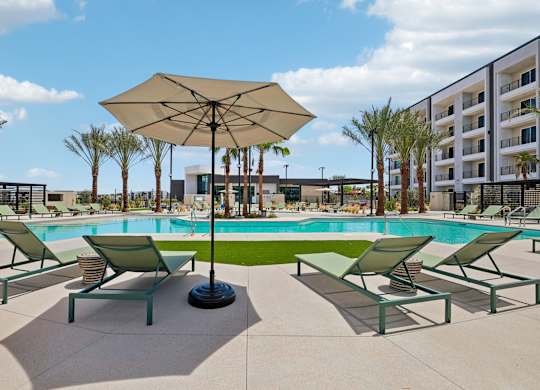 A sunny day at the pool with lounge chairs and an umbrella.