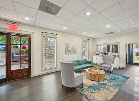 Modern office waiting area with teal sofa, gray chairs, and wood coffee table.