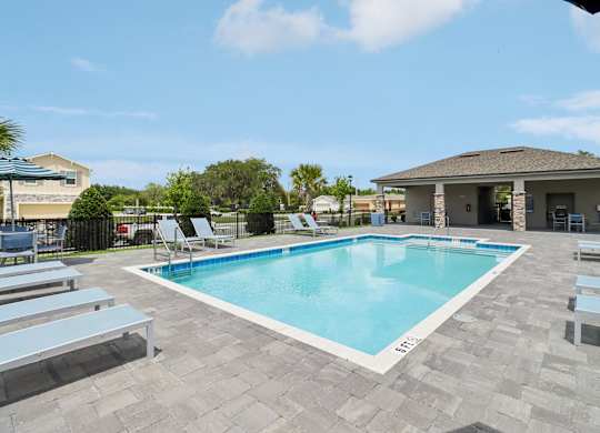 A pool surrounded by lounge chairs and a building in the background.