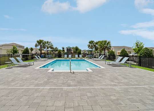 A swimming pool surrounded by a paved area and lounge chairs.