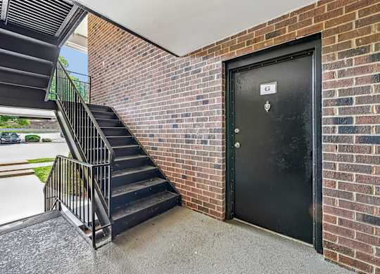 A black door with a white sign on it is on a brick wall.