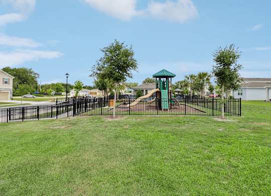A playground with a green slide and a black fence.
