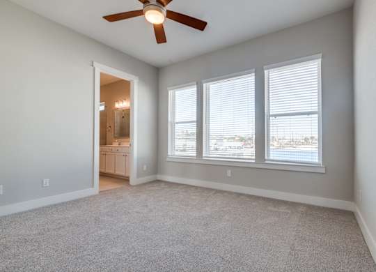 Luxury Three-Bedroom Homes for Rent in Houston, TX - East Heights - Carpeted Bedroom with Large Windows, Soft Grey Walls, Attached Bathroom, and Ceiling Fan.