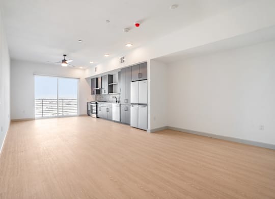 A large empty room with wooden floors and a kitchen area in the background.