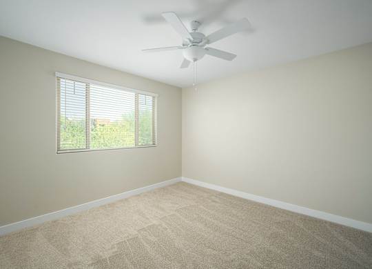 A room with a ceiling fan and a window with blinds.