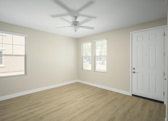 A room with a white door, a ceiling fan, and a window with blinds.