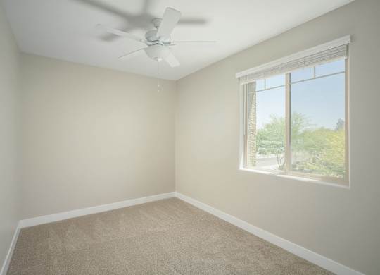 A room with a ceiling fan and a window showing a view of trees.