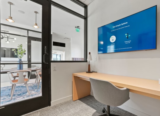 a desk in an office with a large screen on the wall