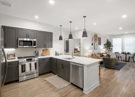 Apartments for Rent in Castle Rock, CO - Alana - Kitchen with Luxury Plank Flooring, Hanging Light Fixtures, Kitchen Island, Quartz Counters, Brown Cabinets, White Tile Backsplash, and Stainless-Steel Appliances