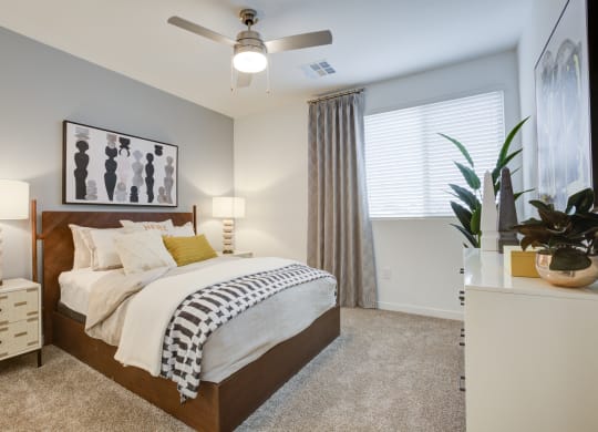 One-Bedroom Apartments in South Scottsdale, AZ - Lucent Scottsdale - Spacious Bedroom With Carpeted Flooring, Bed, Nightstands With Lamps, White Dresser, Ceiling Fan, And Window With Blinds.