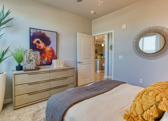 South Scottsdale Apartments - Lucent Scottsdale - Spacious Bedroom With Carpeted Flooring, Bed, Dresser, Arts, and Plants