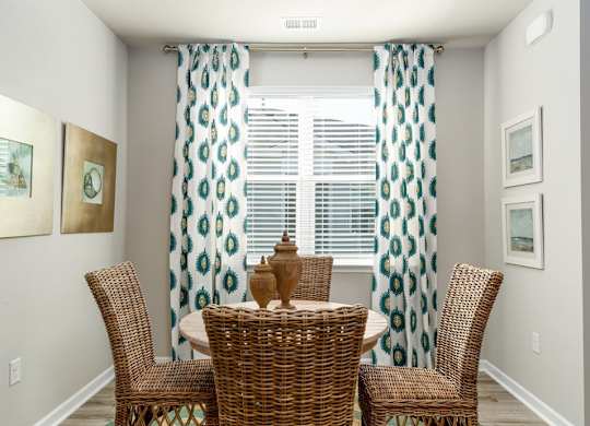 a round table with four chairs in front of a window with curtains