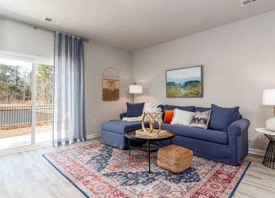 Houses for Rent in Myrtle Beach - The Palmer at Carolina Forest - Living Room with a Blue Sectional Couch, a Large Rug, Vinyl Plank Flooring, and a Sliding Glassdoor