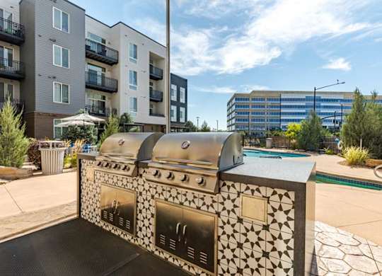 an outdoor grill with a pool and an apartment building in the background