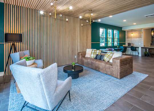 Vancouver, WA Luxury Apartments for Rent - Autumn Grove - Clubhouse with Carpeted Flooring, Leather Sofa, Wingback Armchairs, Coffee Table, Wooden Panel Walls, and Floor-to-Ceiling Windows.