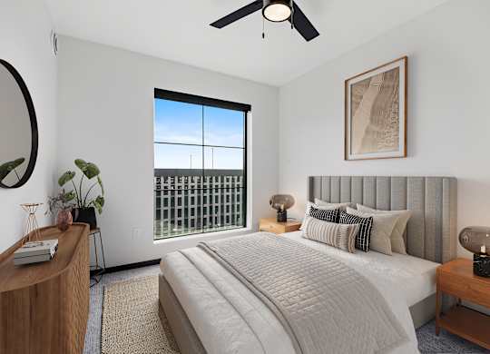A bedroom with a large bed, a ceiling fan, and a window with a view of a fence.