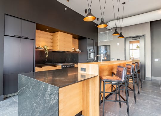 Apartments in Bloomington, MN for Rent - Carbon31 - Kitchen with Contrasting Black and Wooden Tones, Quartz Countertops, a Large Island with Bar Chairs, and Pendant Lights