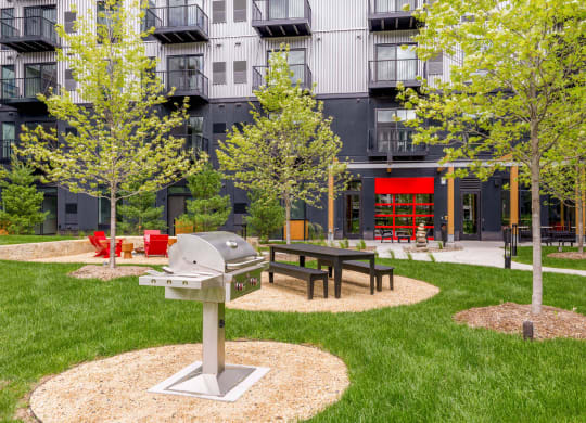 a picnic area with a grill and trees in front of an apartment building
