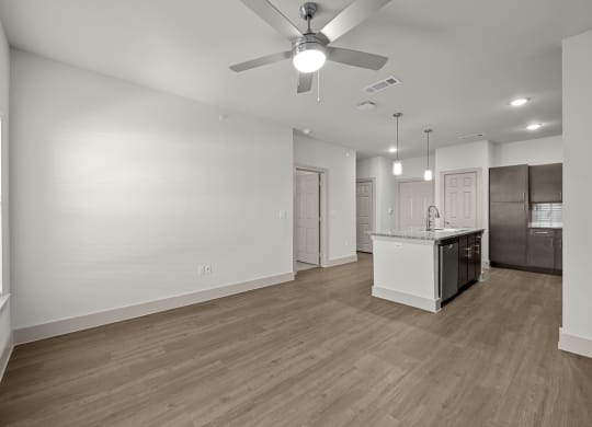 an empty living room with a kitchen and a ceiling fan