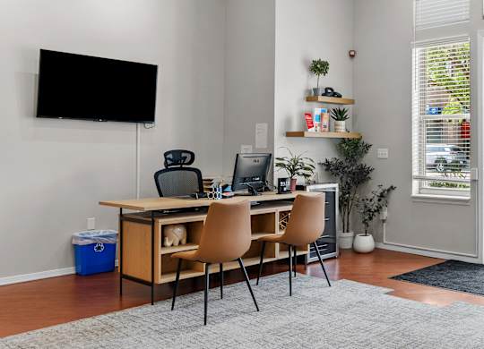 A room with a desk, chairs, and a TV mounted on the wall.