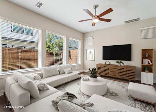 A living room with a white couch, a flat screen TV, and a ceiling fan.